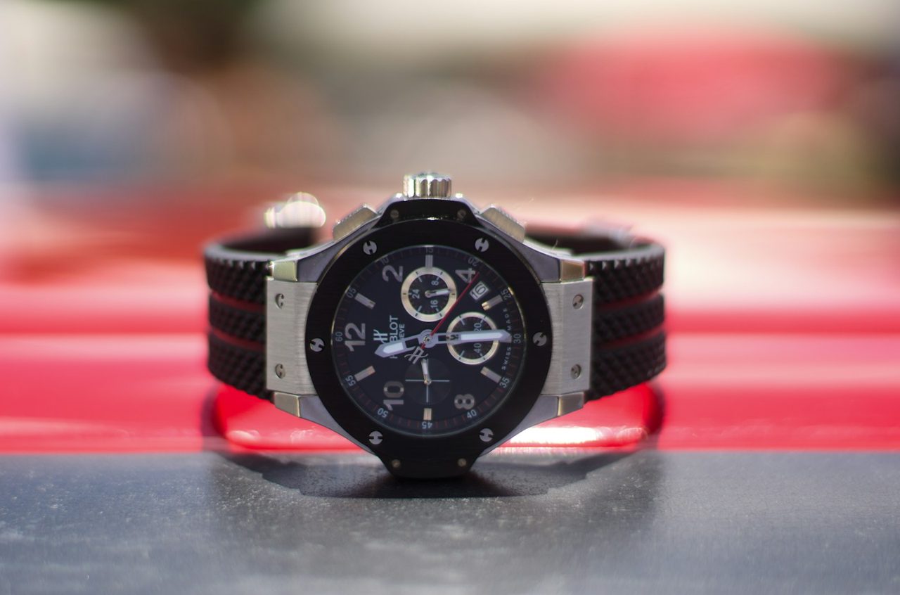 Hublot Big Bang Chronograph mit schwarzer Lünette und schwarz-rotem Gummiband vor rotem, unscharfem Hintergrund