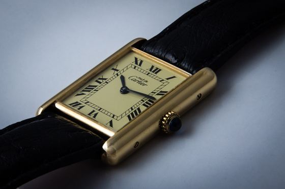Rechteckige Cartier Tank mit goldfarbenem Gehäuse, cremefarbenem Zifferblatt mit römischen Ziffern, Saphir-Cabochon an der Krone und schwarzem Lederband