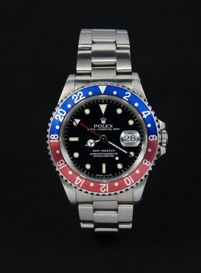 Stählerne Rolex GMT-Master mit rot-blauer Aluminiumlünette, schwarzem Zifferblatt und Oyster-Band vor schwarzem Hintergrund