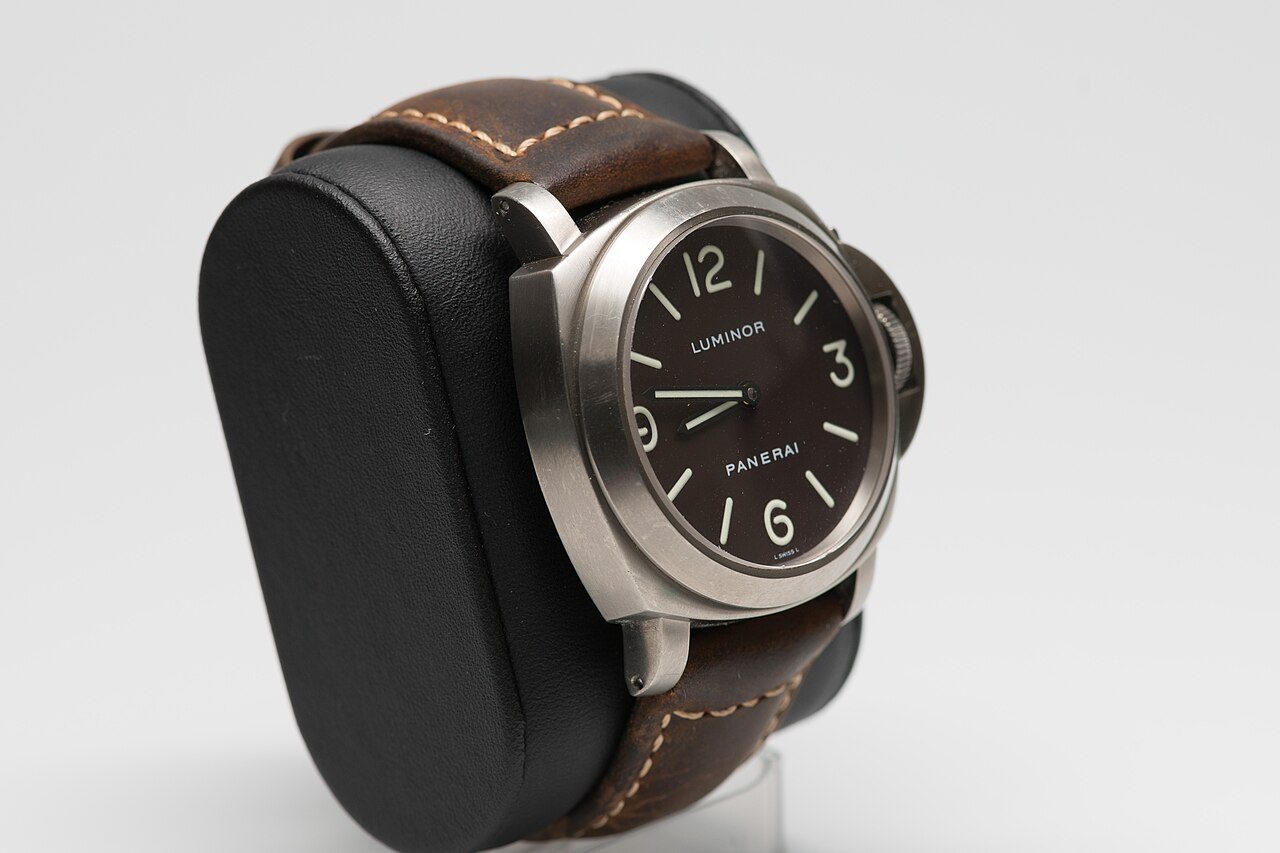 Panerai Luminor mit matt gebürstetem Gehäuse, braunem Zifferblatt und Kronenbrücke auf braunem Lederband, schräg von der Seite auf einem Uhrenkissen