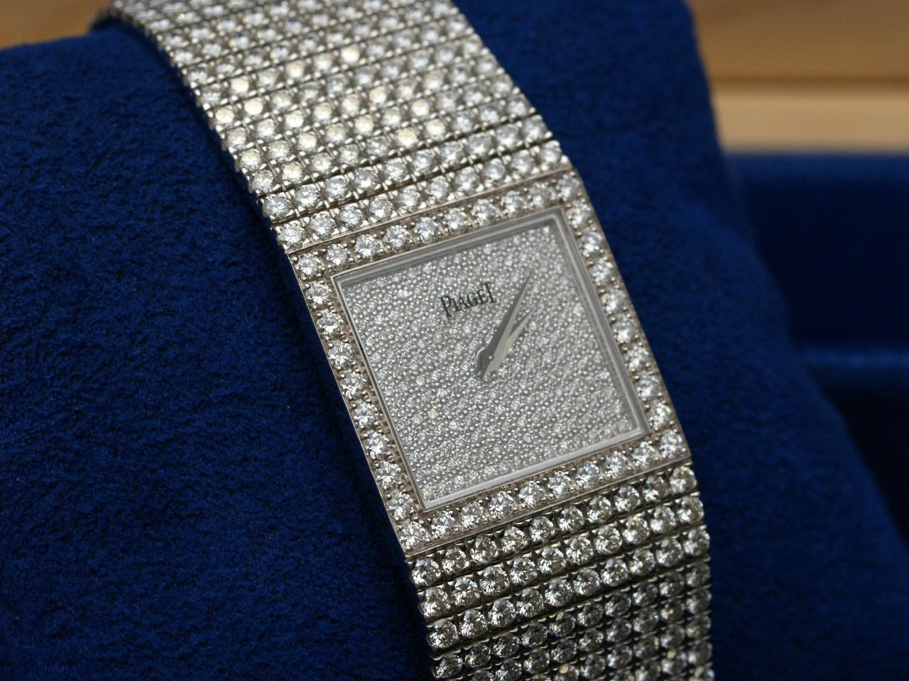 Quadratische Piaget-Armbanduhr mit vollständig diamantbesetztem Zifferblatt, Lünette und Gliederarmband, auf einem dunkelblauen Samtkissen.