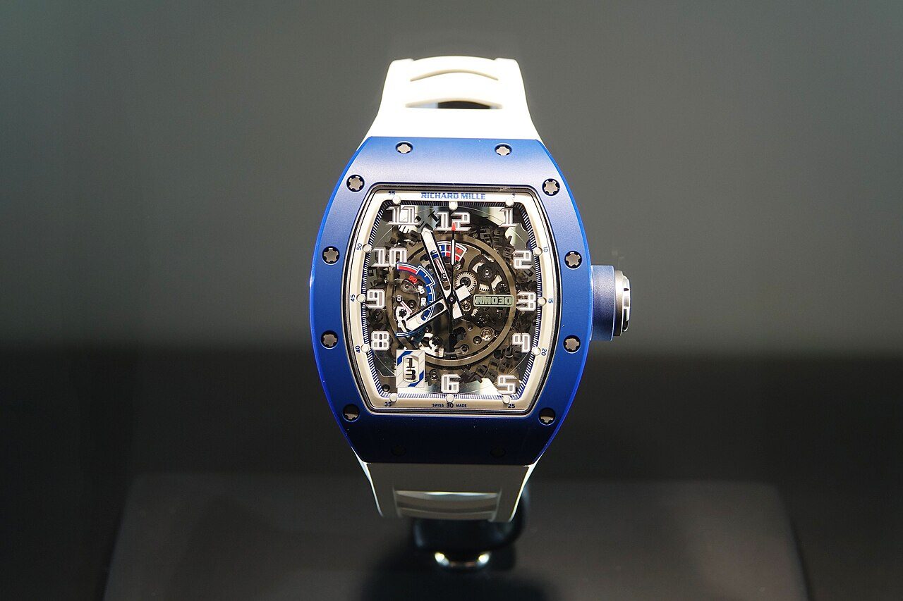 Armbanduhr von Richard Mille mit tonneauförmigem blauem Gehäuse, sichtbaren Schrauben an der Lünette, offenem Skelett-Zifferblatt und weissem Kautschukband