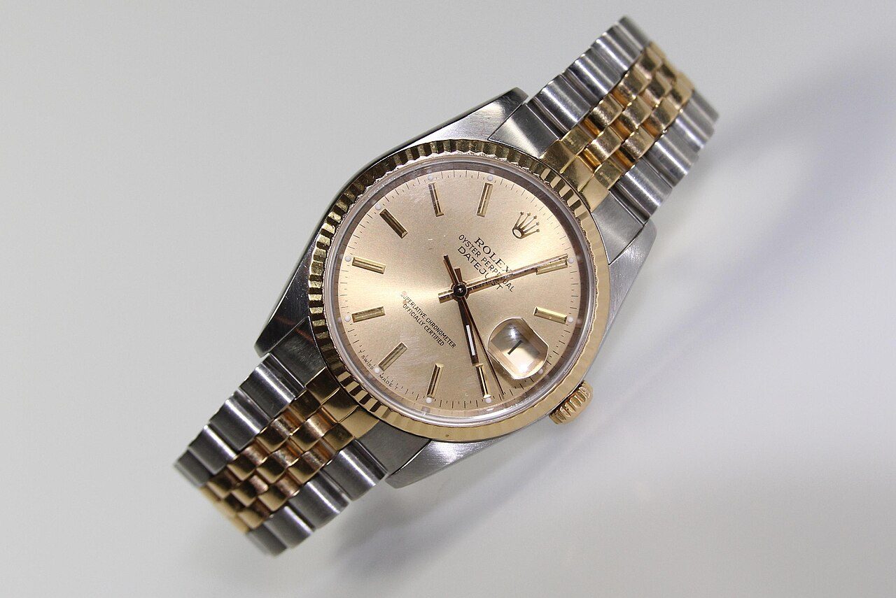 Rolex Datejust mit champagnerfarbenem Zifferblatt, geriffelter Goldlünette, Datumsfenster mit Lupe und zweifarbigem Jubilee-Armband auf hellem Hintergrund