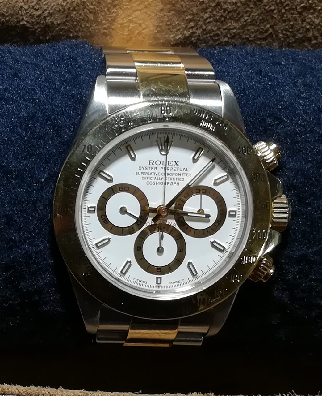 Rolex Daytona aus Stahl und Gold mit weissem Zifferblatt, goldfarbenen Hilfszifferblättern und Tachymeter-Lünette auf einem blauen Uhrenkissen
