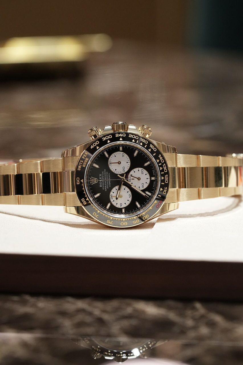 Rolex-Daytona-Chronograph aus Gelbgold mit schwarzer Tachymeter-Lünette, schwarzem Zifferblatt, drei hellen Hilfszifferblättern und goldenem Gliederband auf einem weissen Präsentationskissen