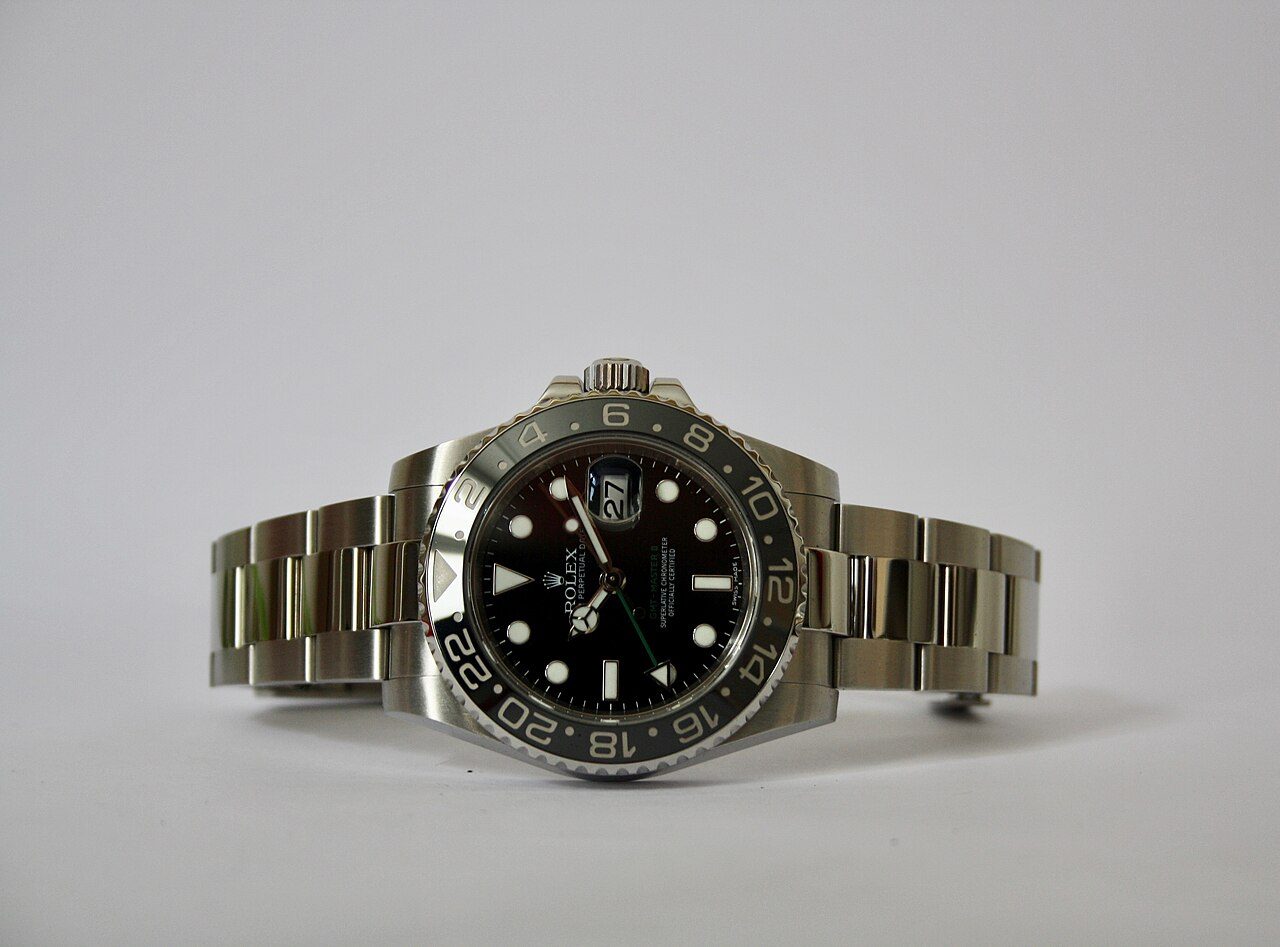 Stählerne Rolex GMT-Master II mit schwarzer Keramiklünette und grünem 24-Stunden-Zeiger, liegend vor hellgrauem Hintergrund