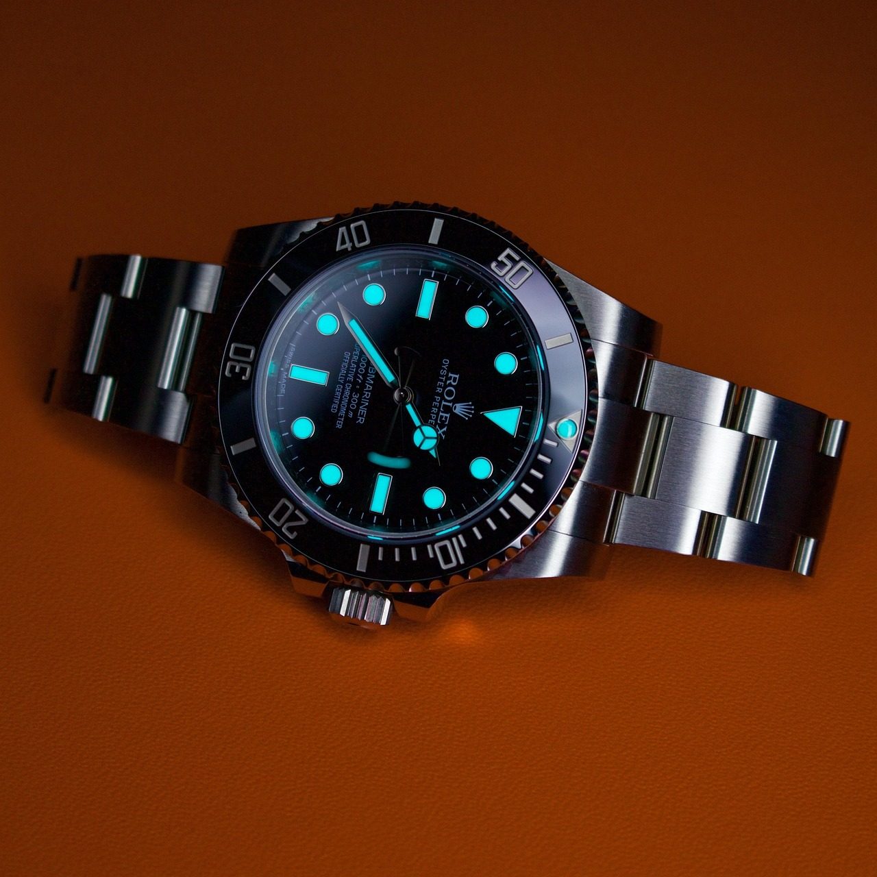 Rolex Submariner aus Stahl mit schwarzer Lünette und grün leuchtenden Indexen vor orangefarbenem Hintergrund