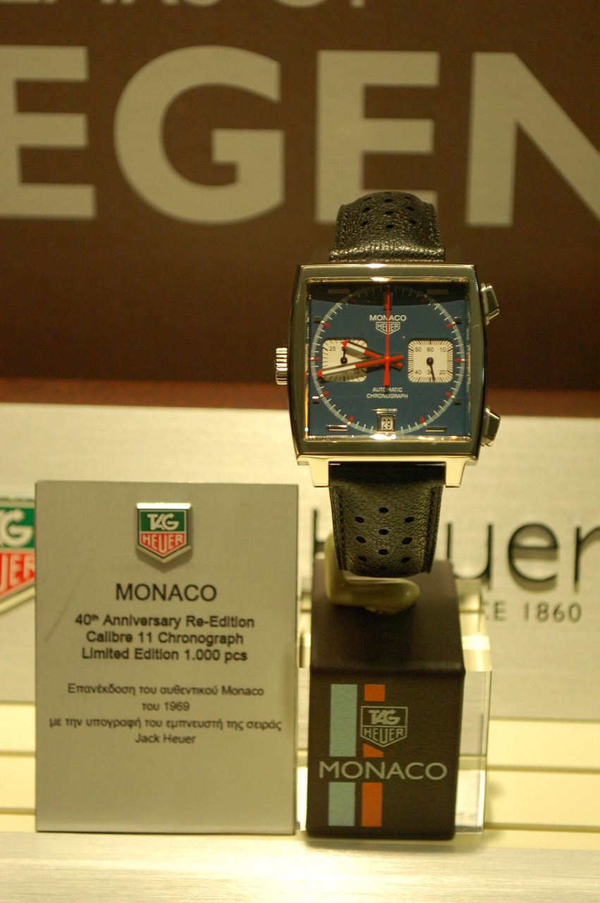 Quadratische TAG Heuer Monaco mit blauem Zifferblatt, zwei weissen Hilfszifferblättern und rotem Sekundenzeiger auf einem Ständer in einer Vitrine