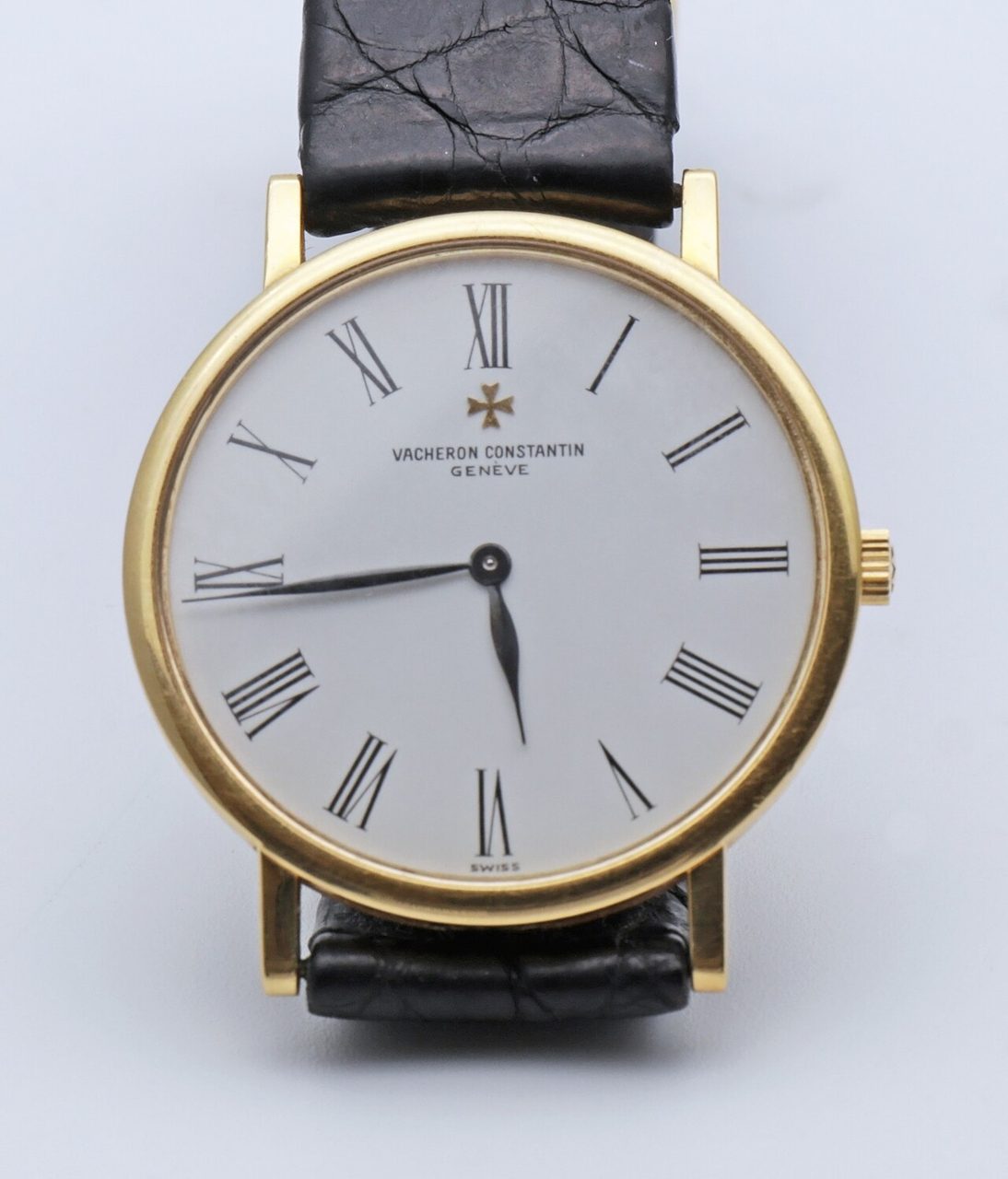 Goldene Armbanduhr mit weissem Zifferblatt, römischen Ziffern, Malteserkreuz und der Aufschrift «Vacheron Constantin Genève» an einem schwarzen Lederarmband